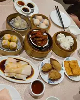 A top-down, overhead shot of a dim sum spread on a restaurant table, featuring various bamboo steamers and plates containing dumplings, buns, and chicken feet.