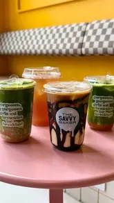 A bright, casual shot of four different iced drinks lined up on a pink table, showcasing the new summer menu at a cafe.