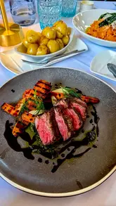 A montage video showcasing the summer evening dining experience at The Pump Room Restaurant in Bath, featuring shots of the elegant dining room, various dishes including steak and pasta, and the adjacent Roman Baths.