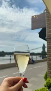 A short, visually appealing montage showcasing a lunch experience at a riverside restaurant in London. The video features shots of the terrace, the view of Hammersmith Bridge, and a variety of dishes including beef tartare, ceviche, ravioli, and a chocolate dessert, all accompanied by champagne.