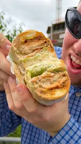 Two creators review sandwiches from Fat Pats in Manchester, highlighting the unique collection process from a 'bin alley' and providing a taste test of the hot honey fried chicken sandwich and the Philly cheesesteak.
