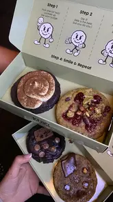 A short, aesthetic montage showcasing a cookie shop called Kuki, highlighting their fresh cookie selection and the concept of dipping cookies in milk.