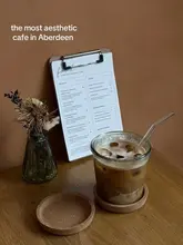 A minimalist, aesthetic shot of an iced coffee and a menu on a wooden table at a cafe in Aberdeen. The image uses a warm, earthy color palette to convey a cozy and inviting atmosphere.