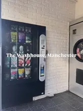 A shot of the entrance to The Washhouse in Manchester, which is designed to look like a laundrette to disguise the speakeasy bar inside. The image features a vending machine and a washing machine door, setting the scene for the hidden venue concept.