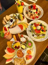 A vibrant, well-composed overhead flat-lay of a brunch spread featuring various dishes including waffles, French toast, a full breakfast, shakshuka, and smoothies.
