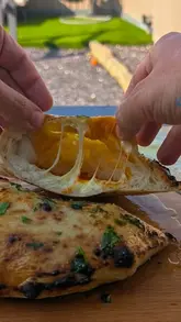 A high-quality, close-up shot of a homemade garlic cheese and nduja pizza pocket being pulled apart, showcasing a satisfying cheese stretch and crispy texture.