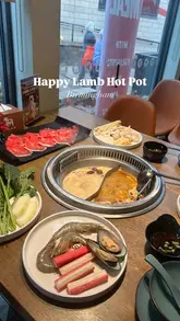 A top-down shot of a hot pot dining experience at Happy Lamb Hot Pot in Birmingham, featuring a duo broth pot, raw beef, seafood, and vegetables.