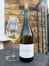 A simple, amateur-style photograph of a bottle of Brookdale Chenin Blanc and a glass of white wine, placed on a dark surface against a brick wall.