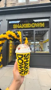 A promotional shot of a milkshake held in front of the Shakedown storefront in Edinburgh, likely during the Fringe festival, showcasing the venue's branding.