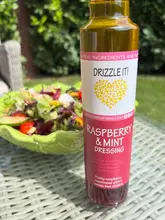A clean, well-lit product shot featuring a bottle of Raspberry & Mint Dressing from Lincolnshire Drizzle Co, positioned in the foreground with a fresh, colourful salad blurred in the background to provide context.