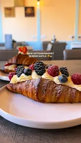 A short, visually focused reel showcasing a new artisan bakery in Newcastle. The video features close-up shots of various pastries, including fruit-topped croissants, a tiramisu danish, and a blueberry brioche bun, alongside specialty coffees. It concludes with a shot of the bakery's exterior.