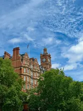 A clear, daylight shot of a historic red-brick building with a clock tower in Marylebone, London, framed by trees against a blue sky.