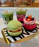 A high-quality, close-up shot of two gourmet donuts and two iced matcha lattes served on a branded tray at Donutelier. The image focuses on the vibrant colors and textures of the pastries and drinks, highlighting the aesthetic appeal of the products.