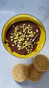 A concise, top-down recipe video demonstrating the preparation of a homemade pistachio and chocolate dessert dip, served with cookies.