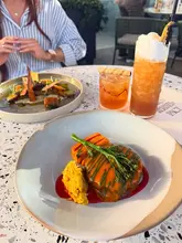 A bright, inviting shot of a table spread at a rooftop venue, featuring a main course, a side dish, and cocktails, capturing a relaxed dining atmosphere.
