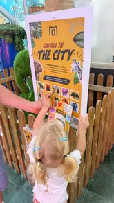 A mother and her young child explore a free 'Safari in the City' event at Midsummer Place shopping centre, participating in interactive activities like drawing, examining animal artifacts, and collecting stamps for a competition.