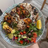 A top-down, overhead shot of a homemade meal consisting of grilled chicken, charred courgettes, a fresh Greek-style salad, and flatbread.