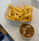 A simple, top-down, eye-level snapshot of a portion of takeaway chips and a pot of curry sauce in a cardboard box, set against a plain white counter.