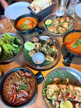 A high-quality, overhead flat-lay photograph of a large Indian feast at a restaurant, featuring various curries, sides, and breads arranged on a table.