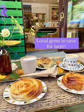 A cozy, rustic flat-lay shot of coffee and pastries, including cinnamon rolls and cheese and olive acma, set on a tray against an outdoor cafe backdrop with flowers, capturing a relaxed, local cafe vibe.