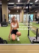 A mirror selfie taken in a gym setting featuring a fitness influencer holding a protein drink.
