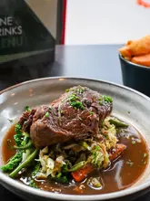 A close-up, appetizing shot of a slow-cooked beef shoulder dish served with vegetables and a rich gravy, presented in a rustic bowl.
