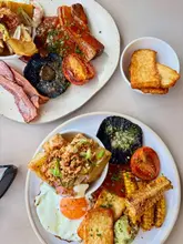A high-quality overhead shot of a brunch spread featuring a Full English breakfast with pork belly and a Full Veggie breakfast with sweetcorn ribs and potato hash, served at a cafe.