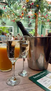 A vibrant, music-led reel showcasing a bottomless brunch experience at The Lawn Club. The video features quick cuts of the venue's outdoor seating area, various cocktails, and food items like pizza and fries, interspersed with clips of guests enjoying themselves and dancing on benches.