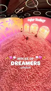 A bright, high-quality shot of an immersive 'House of Dreamers' experience in London, featuring a large pink ball pit. The composition is clean and inviting, effectively showcasing the playful, aesthetic nature of the venue.