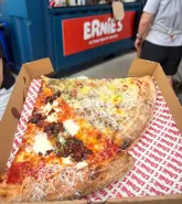 A high-quality, close-up shot of two slices of pizza served in a branded takeaway box. The lighting is natural and bright, highlighting the textures of the cheese, chili, and crust, making the food look fresh and appealing. The composition is tight and focused on the product, effectively showcasing the quality of the pizza.