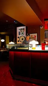 A montage video showcasing the atmosphere of Simone's cocktail club in Liverpool, featuring close-ups of cocktails, a DJ playing vinyl records, and patrons socializing and dancing in a dimly lit, red-hued setting.