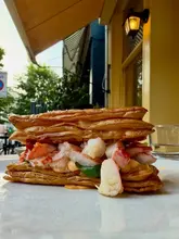 A high-quality, eye-level close-up shot of a lobster pastry roll, showcasing the flaky texture of the pastry and the fresh lobster filling. The lighting is natural and soft, highlighting the appetizing details of the dish against a blurred, clean background.