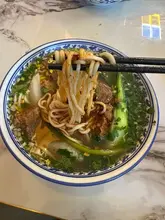 A close-up, top-down shot of a bowl of beef noodle soup being lifted with chopsticks, showcasing the texture of the noodles and the clarity of the broth.