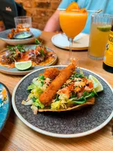 A close-up, angled shot of a prawn tostada and a cocktail at a restaurant, showcasing new summer menu items.