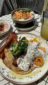 A creator visits Brother Marcus for brunch, showcasing various dishes including a Greek sausage flatbread, halloumi with watermelon, and a yogurt bowl. The video highlights the venue's atmosphere and explains a discount offer available through the First Table app.