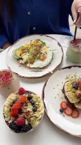 A short, aesthetic montage showcasing a brunch cafe in London. The video features close-ups of various brunch dishes, including avocado toast and smoothie bowls, alongside drinks like matcha and smoothies. It also highlights the cafe's waterside location and outdoor seating area, creating a relaxing and inviting atmosphere.