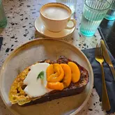 A high-quality, well-lit overhead shot of a brunch dish featuring French toast topped with mascarpone and spiced peaches, served alongside a dirty chai latte on a terrazzo table.