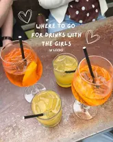 A bright, overhead POV shot of four cocktails on a weathered outdoor table, used to introduce a list of recommended bars in Leeds.