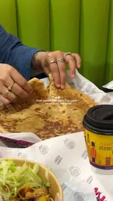 A casual, first-person perspective shot of a meal at Naanstaap, featuring a torn paratha, a takeaway cup, and a salad bowl, captured in a brightly lit, casual setting.