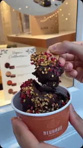 A short, handheld video showcasing a chocolate mousse dessert being served at a Neuhaus store, highlighting the option for milk or dark chocolate.