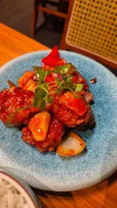 A short, handheld-style video review of YiQi Lah!, a Southeast Asian street food canteen in London's Chinatown. The video features shots of the restaurant's exterior and interior, followed by a montage of various dishes including chicken wings, prawns, and rice, highlighting the vibrant and spicy nature of the food.