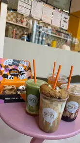 A creator visits The Savvy Baker to showcase their summer drink specials, including a cookie-topped latte, matcha, and iced tea. The video features the creator attempting to make drinks and soft serve, followed by a taste test of the treats and brownies.