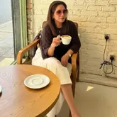 A lifestyle-focused shot of a woman enjoying a coffee in a cafe setting, positioned by a window with a view of the water.