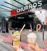 A bright, clear, and well-composed shot of a pistachio sundae and a hazelnut milkshake held in front of a Love Churros London food truck. The image effectively highlights the products in their natural, casual setting.