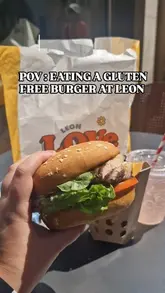 The video features a creator visiting a Leon restaurant to try their newly returned gluten-free burger bun. The footage includes shots of the exterior, the branded packaging, the chargrilled chicken burger, waffle fries, and a raspberry lemonade, all filmed from a first-person perspective while sitting at an outdoor table.