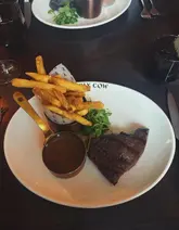 A standard, top-down restaurant shot of a steak dinner featuring a rump steak, fries, and peppercorn sauce. The image captures the meal in a casual dining setting, though the composition is slightly tight and lacks professional polish.