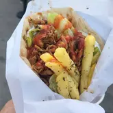 A close-up, eye-level shot of a chicken gyros served in a paper wrapper, featuring fries, lettuce, and sauce, captured at a street food stall.