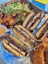 A flat-lay shot of a takeaway order from Groke, featuring smash burgers, loaded fries, and milkshakes in their original packaging.