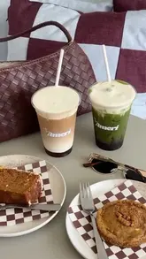 A visually focused reel showcasing the preparation of specialty drinks, including a maple syrup latte and a blueberry coconut matcha, alongside carrot cake and a cookie at The Ameri cafe.