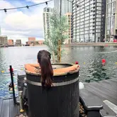 A lifestyle shot featuring a person relaxing in a floating sauna tub at a city dock, highlighting a wellness experience.